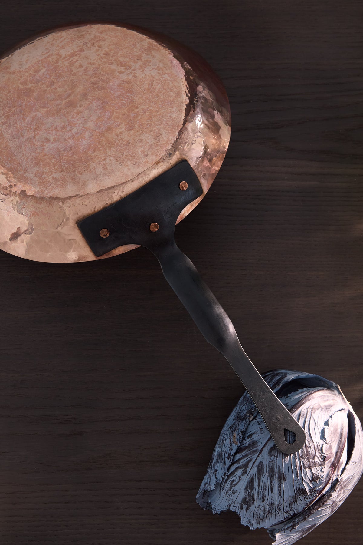 Hand raised copper pan bottom view, handle resting on purple cabbage